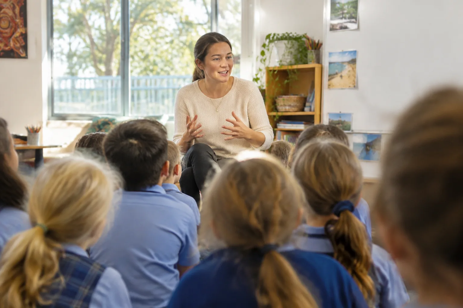 A teacher talking with a group of primary school children seated on a classroom floor