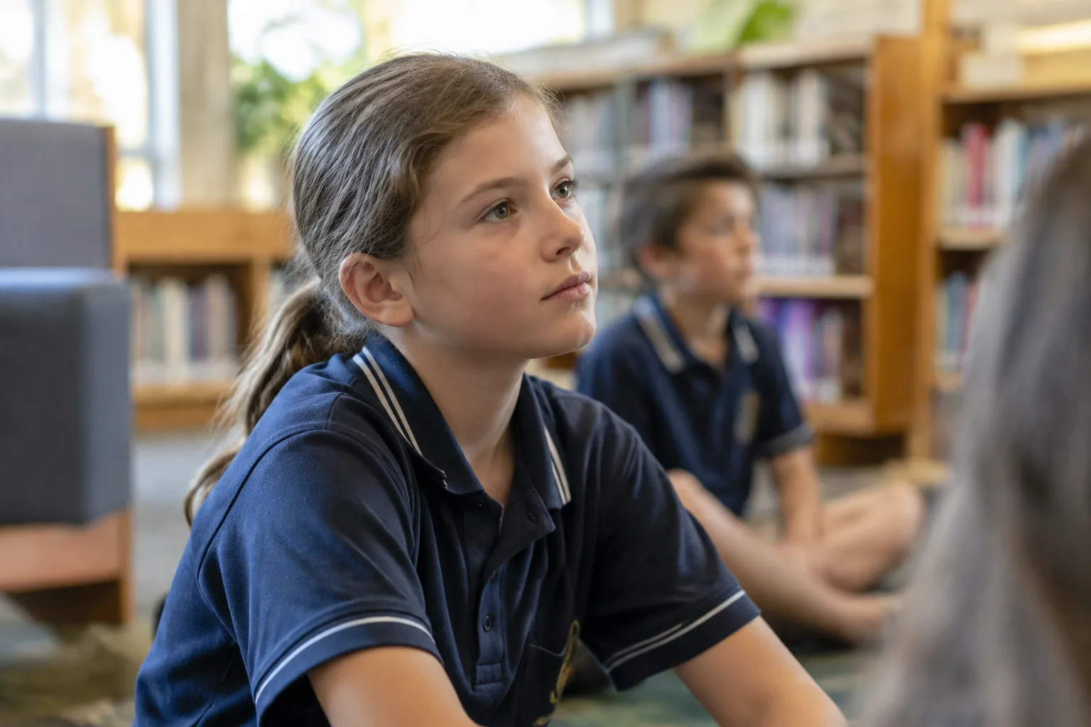 A school-aged girl in a uniform listening in a school library